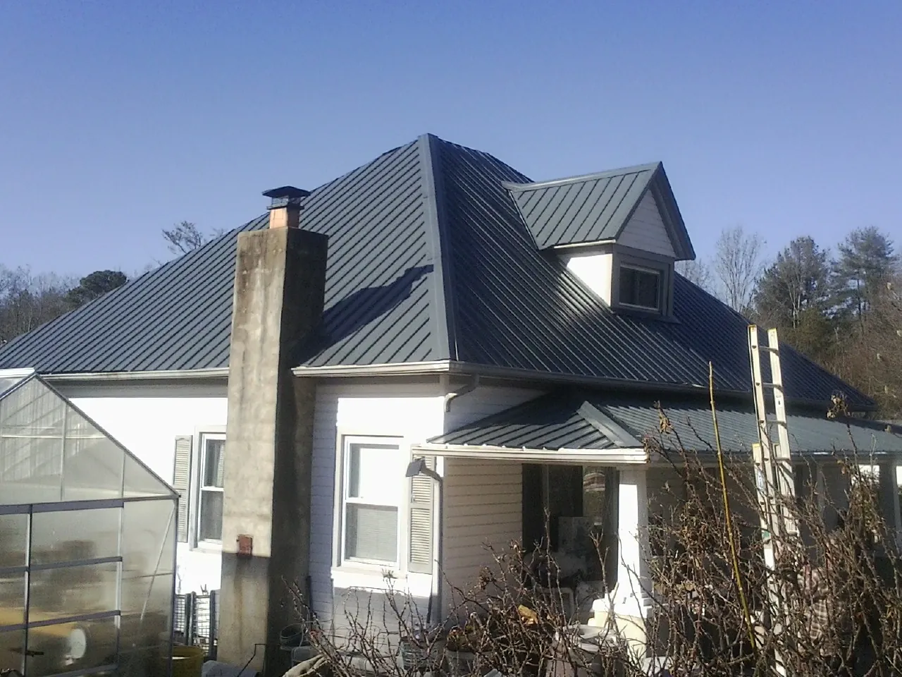 Dark blue standing seam metal roof on a white farmhouse with dormer — Slate & Tile Roof Repair by Roofing Brothers in Sheakleyville