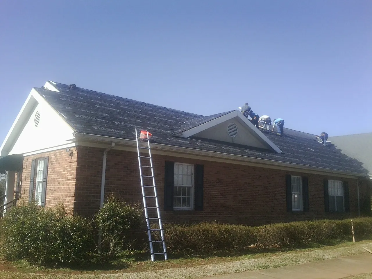 Crew tearing shingles off a brick ranch roof with a ladder set — Emergency Roof Repair work by our crew in Sheakleyville