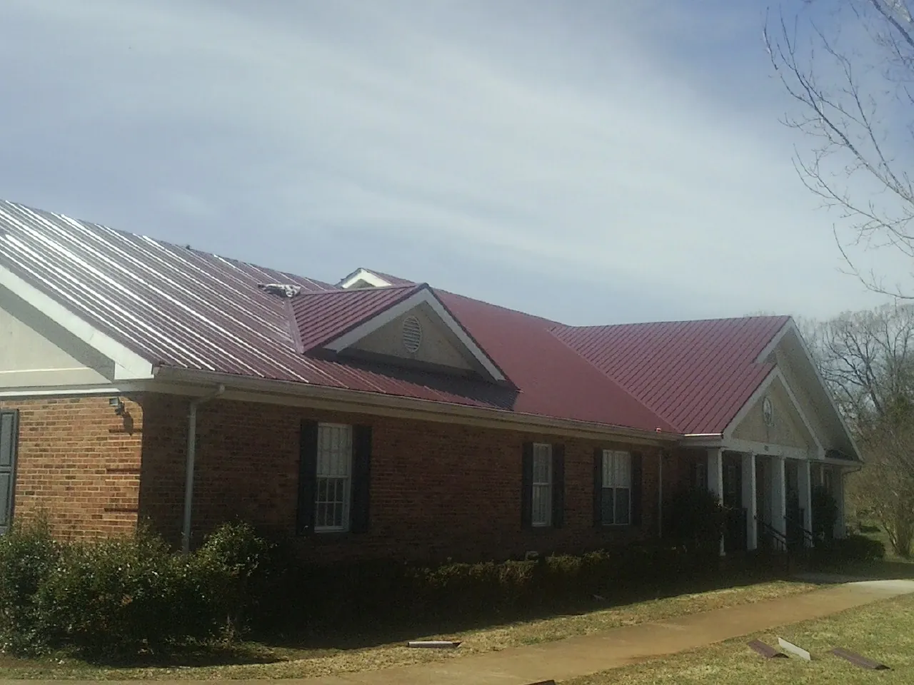 Red metal roof with gabled entries on a long brick building, from a Hail Damage Roof Repair job in Sheakleyville