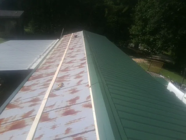 Old rusted panels beside newly installed green metal roofing — Wind Damage Roof Repair by Roofing Brothers in Sheakleyville
