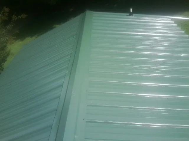 New green metal panels meeting at the ridge of a roof — Flat Roof Repair work by our crew in Sheakleyville