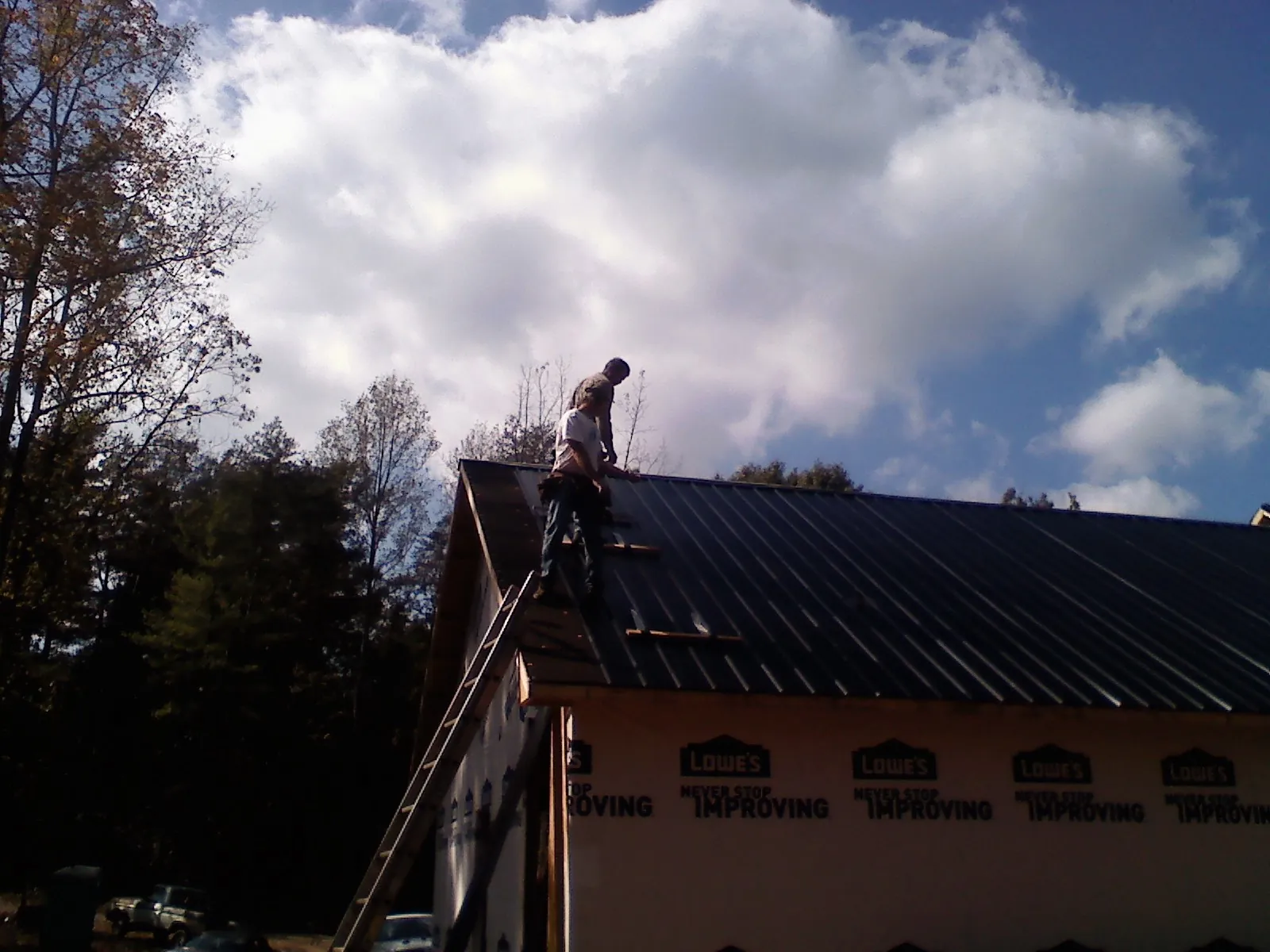 Roofer fastening dark metal panels high against a cloudy sky, from a Roof Inspection job in Sheakleyville