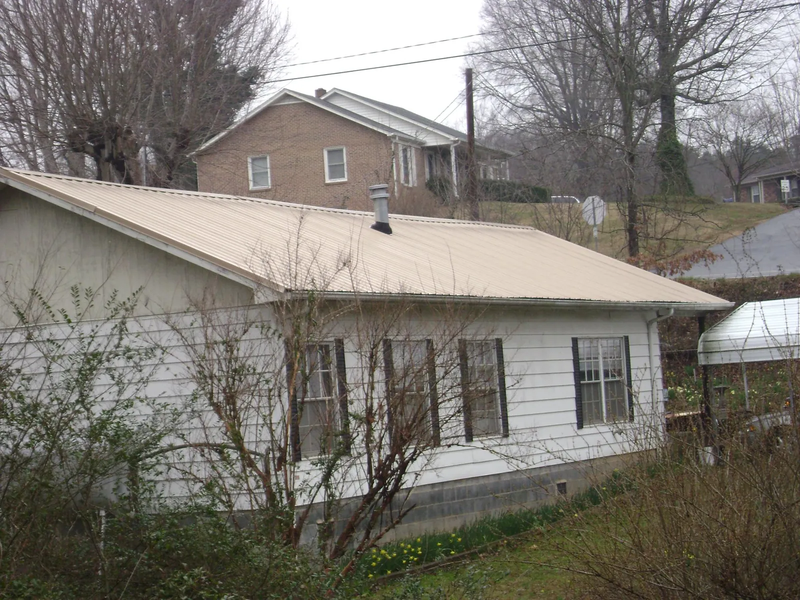 Tan metal roof on a white sided house set into a hillside — Commercial Roofing by Roofing Brothers in Sheakleyville